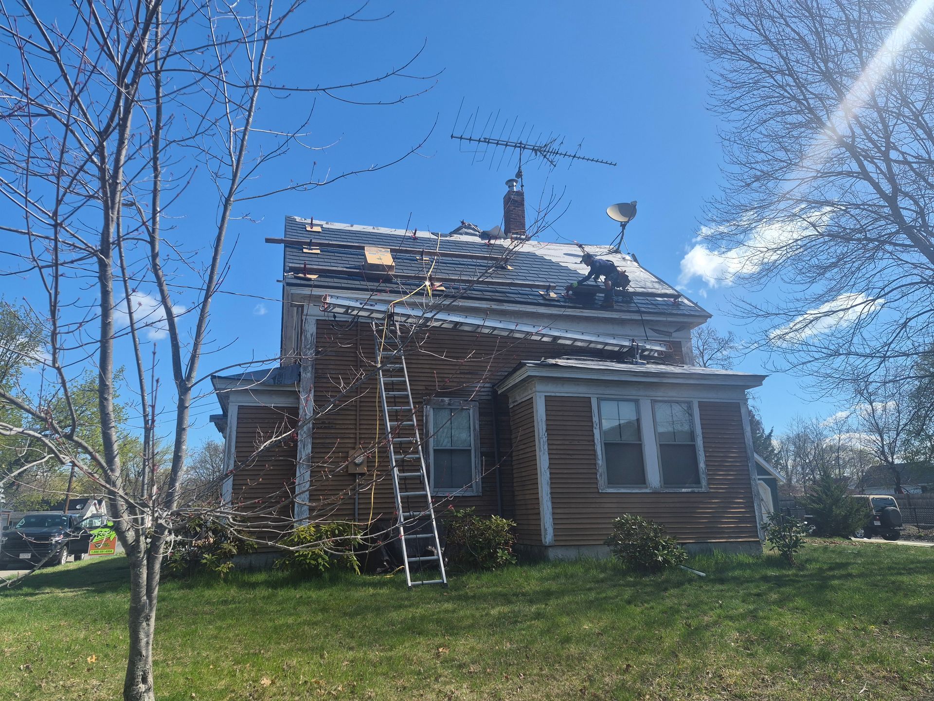 Old brick house with a damaged roof and two ladders in a grassy yard under a bright blue sky
