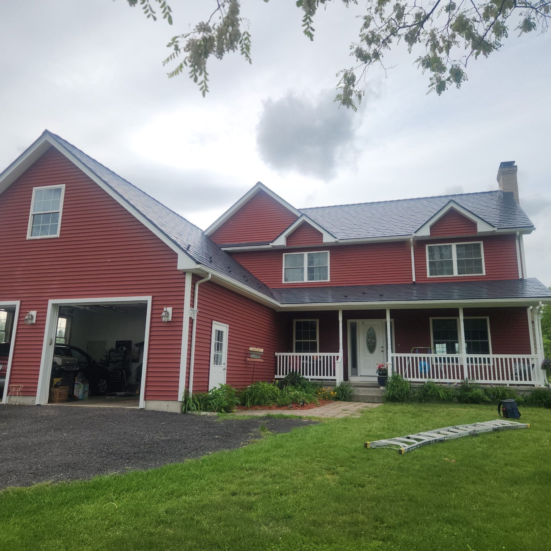 Red two-story farmhouse with white trim, front porch, attached garage, and green lawn under cloudy skies