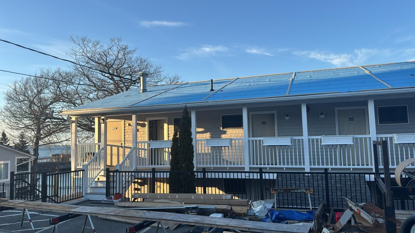 Rowhouse porch with blue tarp-covered roof, white railing, and scattered lumber in front yard.