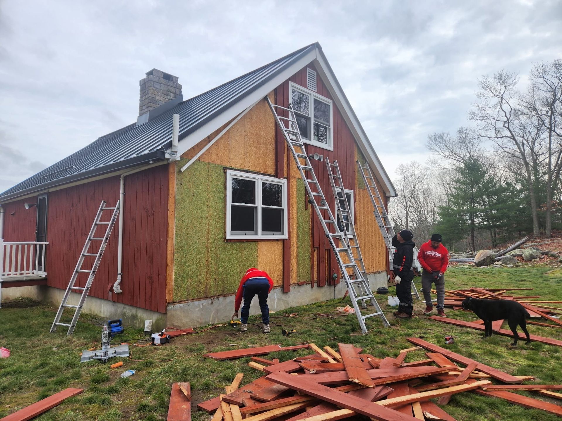 Workers and ladders on a red house exterior during roof and siding repairs