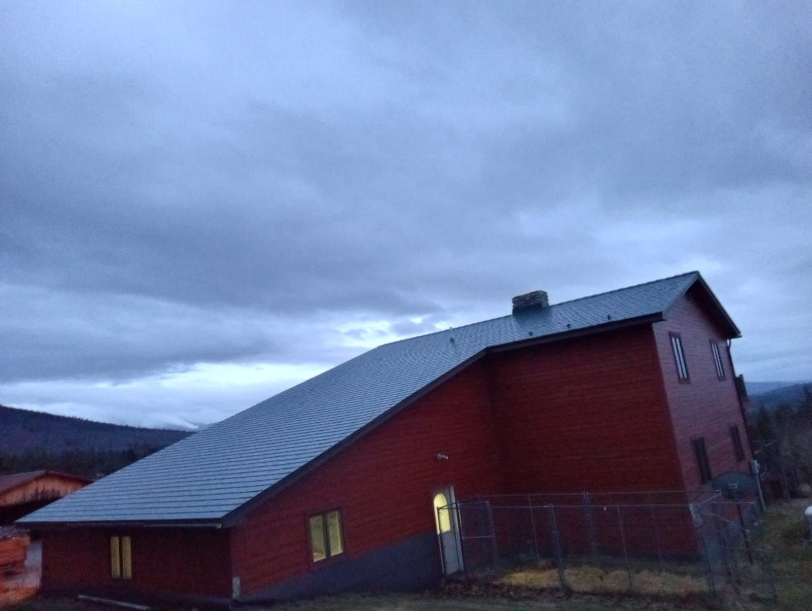 Red building with a sloped metal roof at dusk under a cloudy sky.