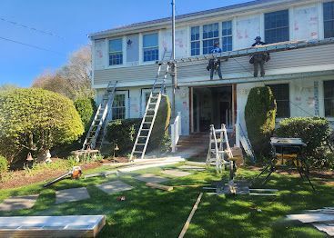 Two-story house with multiple ladders set up in the front yard for exterior work
