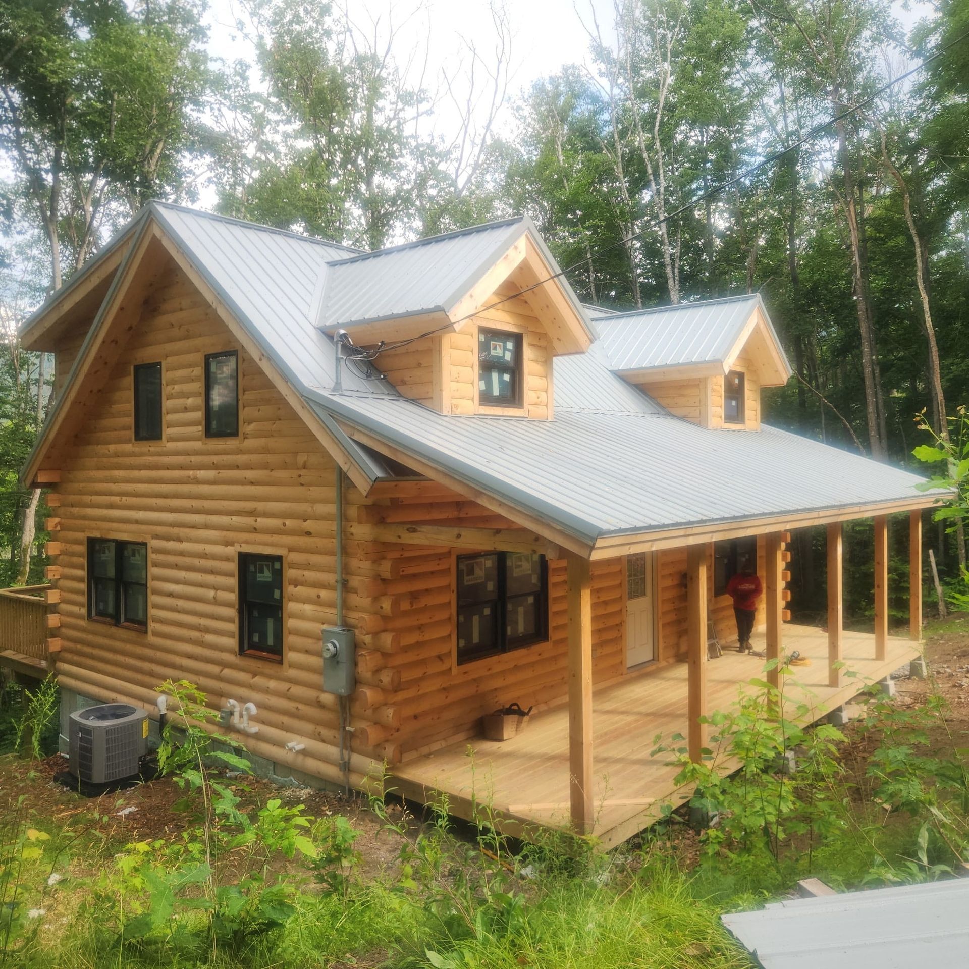 Wooden cabin with metal roof and wraparound porch nestled in a wooded setting