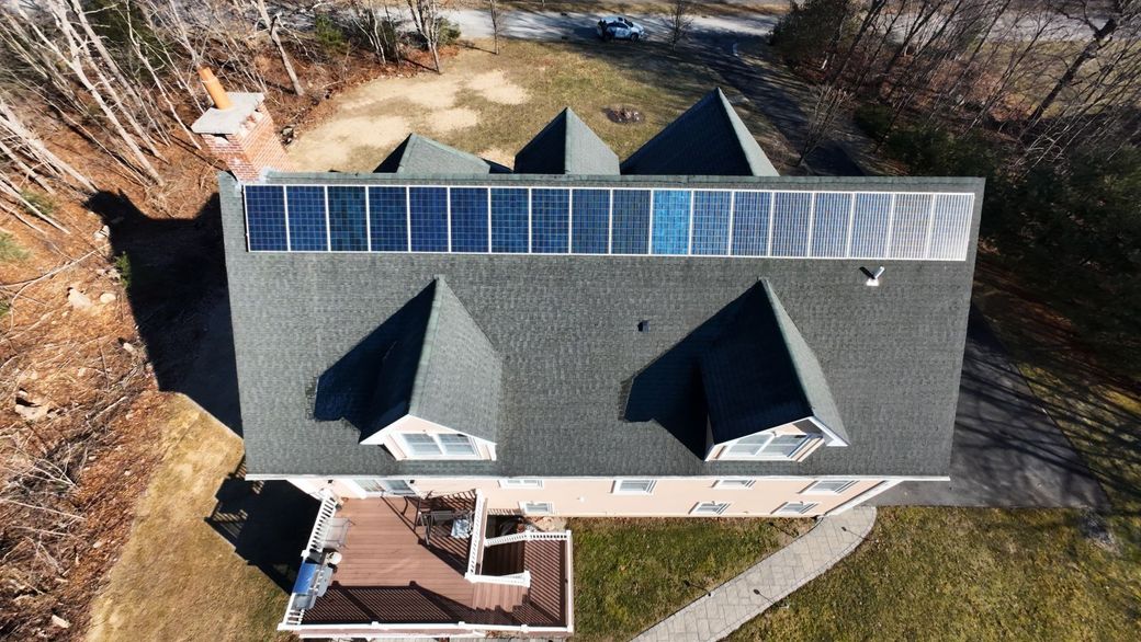 Aerial view of a house with solar panels on the roof and a wooden deck in a wooded area