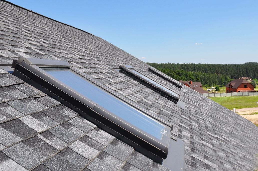 Solar roof skylights on a gray shingled rooftop with a countryside view in the background