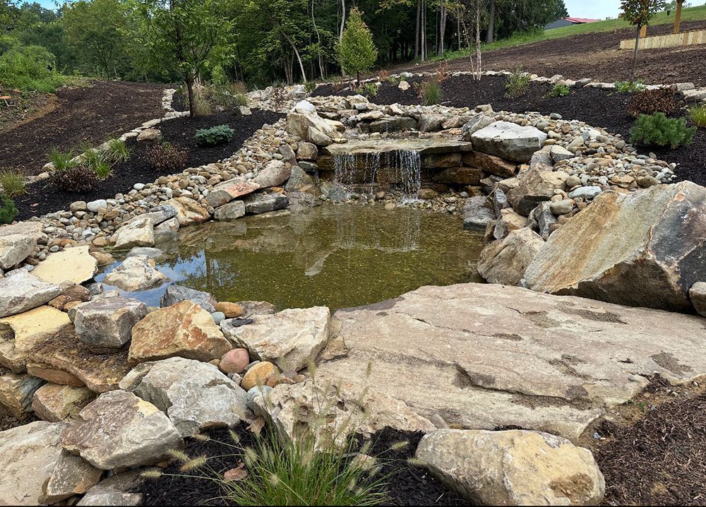Rocky waterfall cascading into a pond, surrounded by boulders and landscaping.