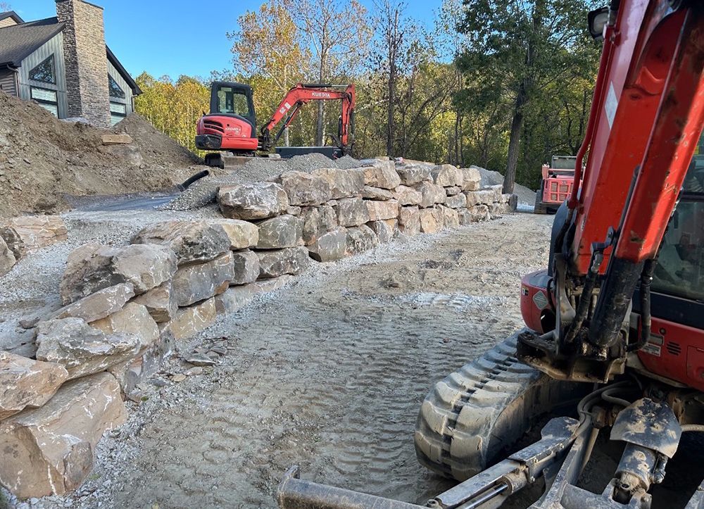 Construction site with rock wall being built; red excavators and machinery.