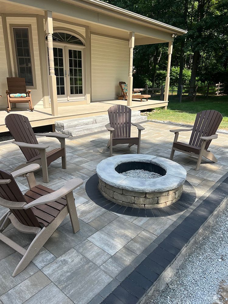 Patio with Adirondack chairs around a stone fire pit, next to a house.