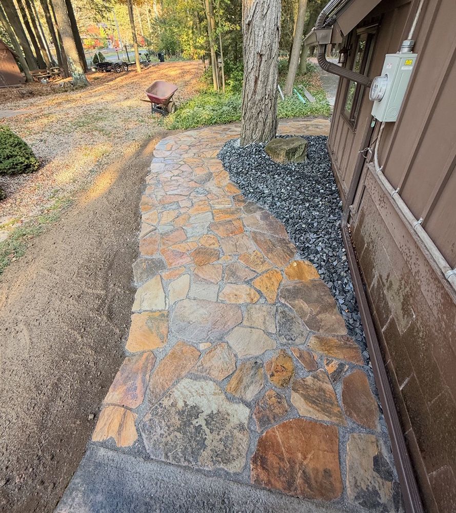 Stone pathway alongside a brown house, next to a bed of black gravel.