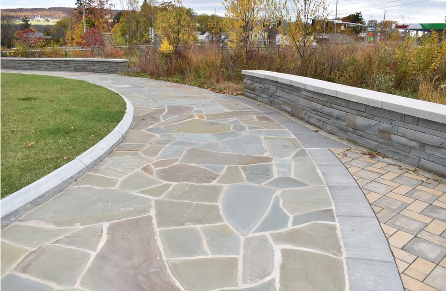 Stone path curves through a park, bordered by grass and a stone wall.