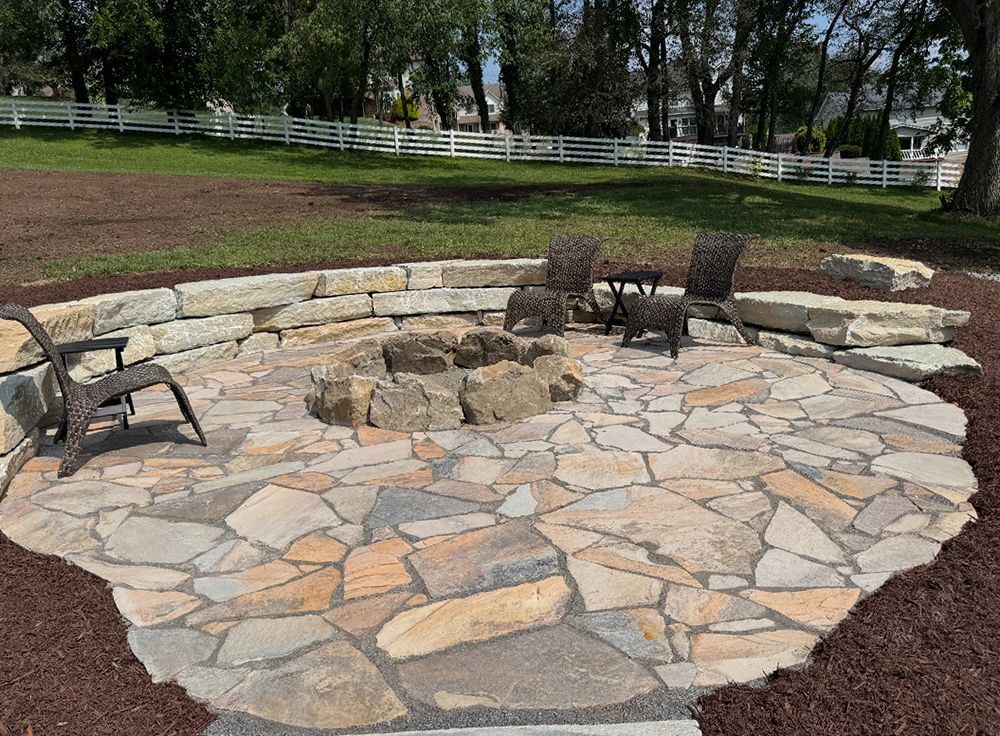 Stone fire pit patio with chairs and stone retaining wall.