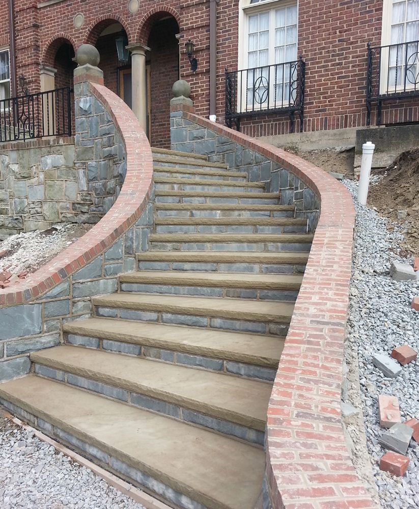 Brick staircase leading up to a red brick building with stone walls and a curved red brick handrail.