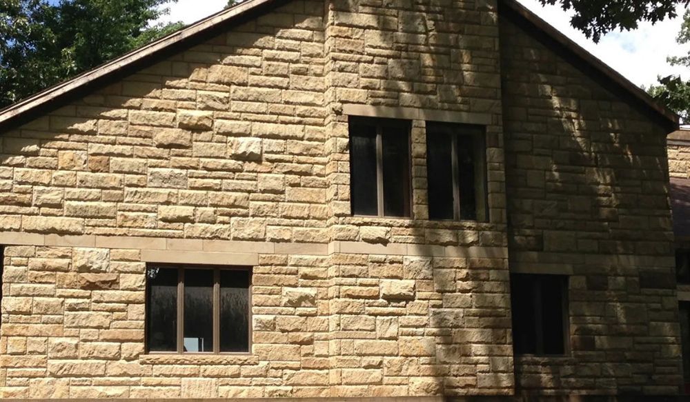 Stone exterior wall with dark windows and a gabled roof, in daylight.