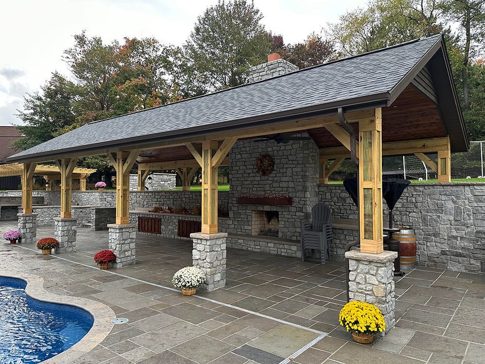 Outdoor pavilion with a stone fireplace, adjacent to a pool, with fall flower arrangements.