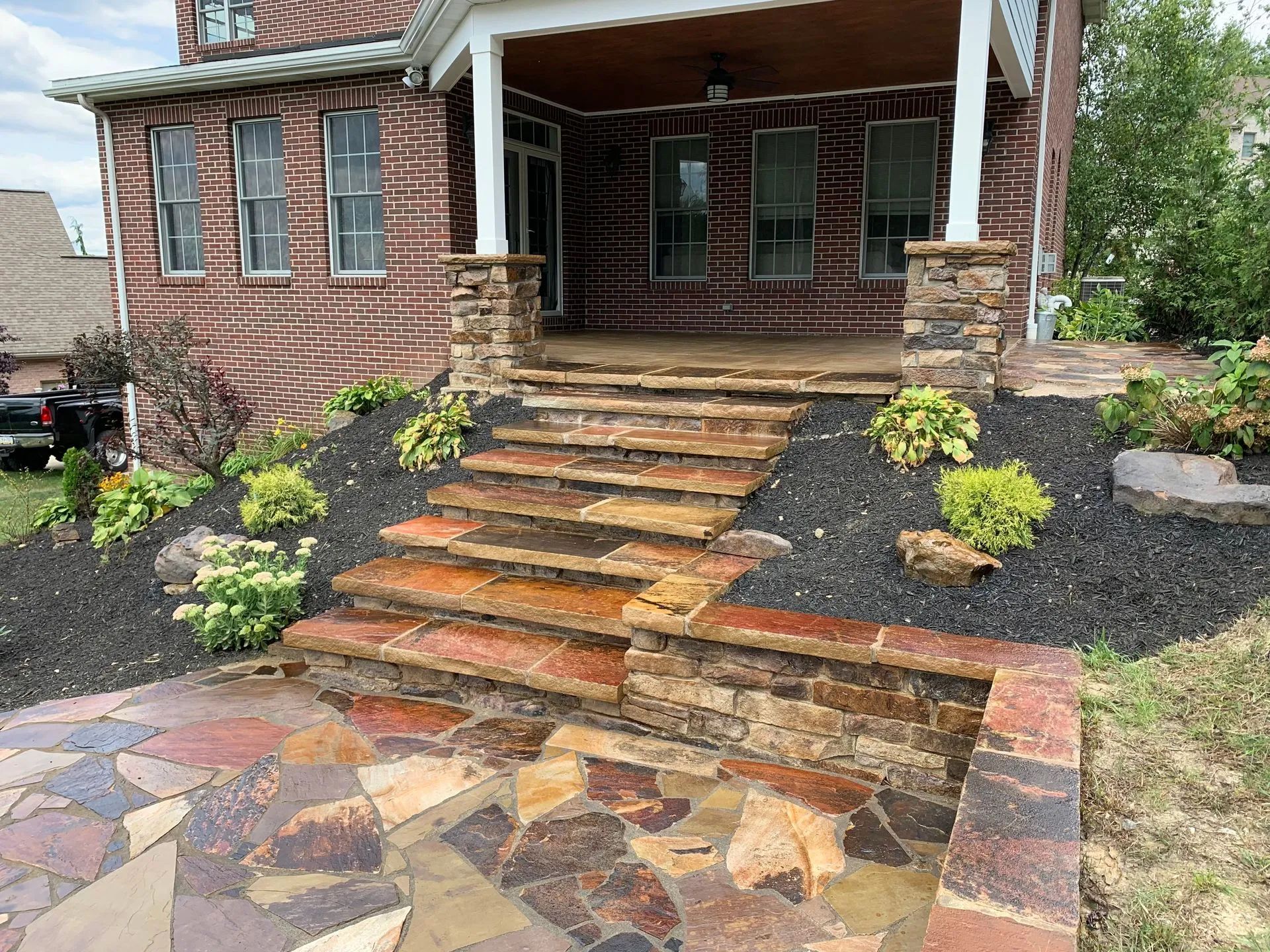 Stone steps and walkway leading to a brick home's porch, surrounded by dark mulch and landscaping.