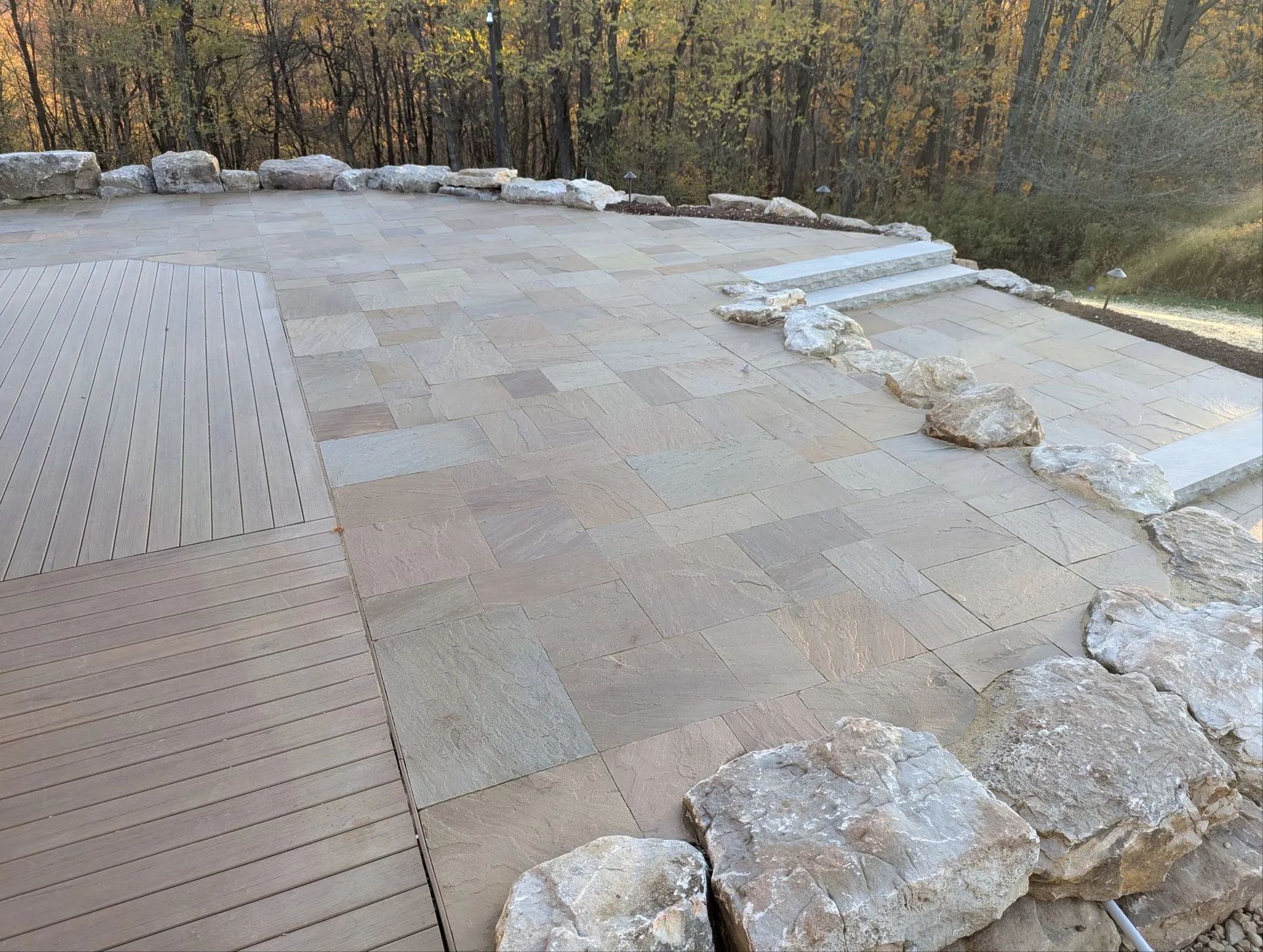 Stone patio with rock border and steps, overlooking trees.