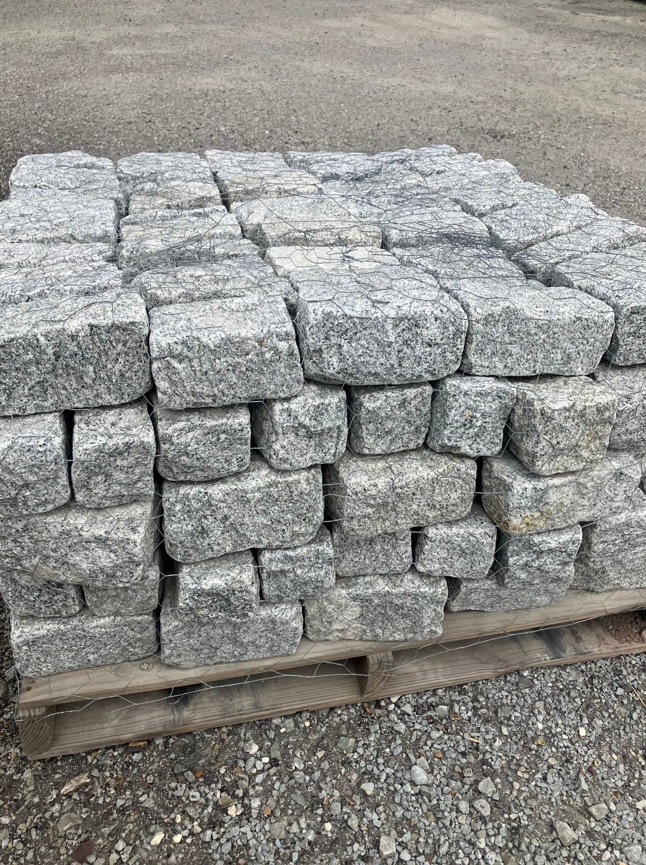 A stack of rectangular, gray granite paving stones on a wooden pallet, outdoors.