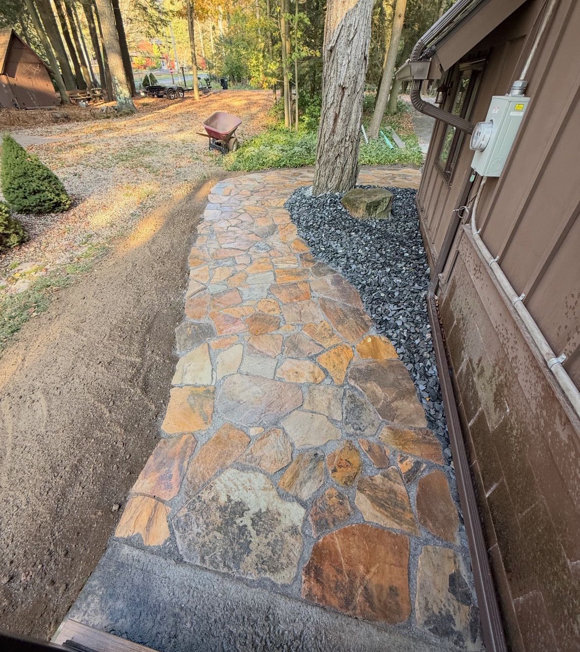 Stone pathway next to a brown house and a tree, with black gravel along the side.