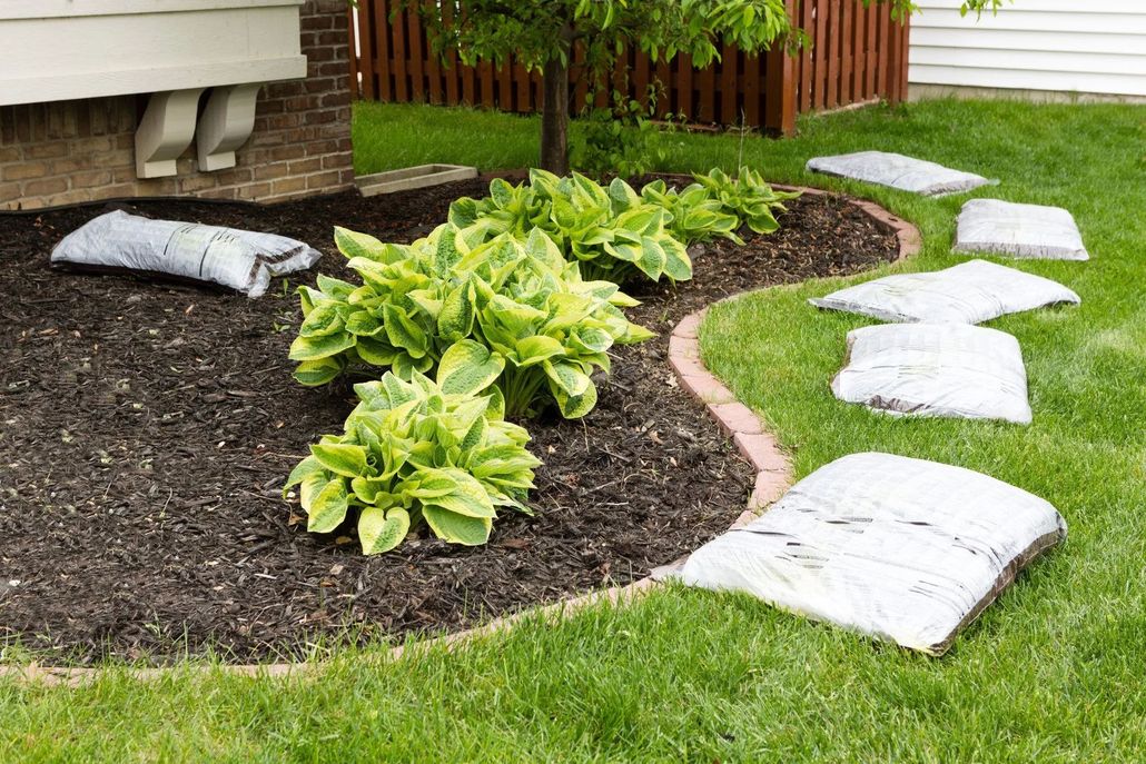 Landscaped flower bed with grey rocks, various plants, and a brick pathway.