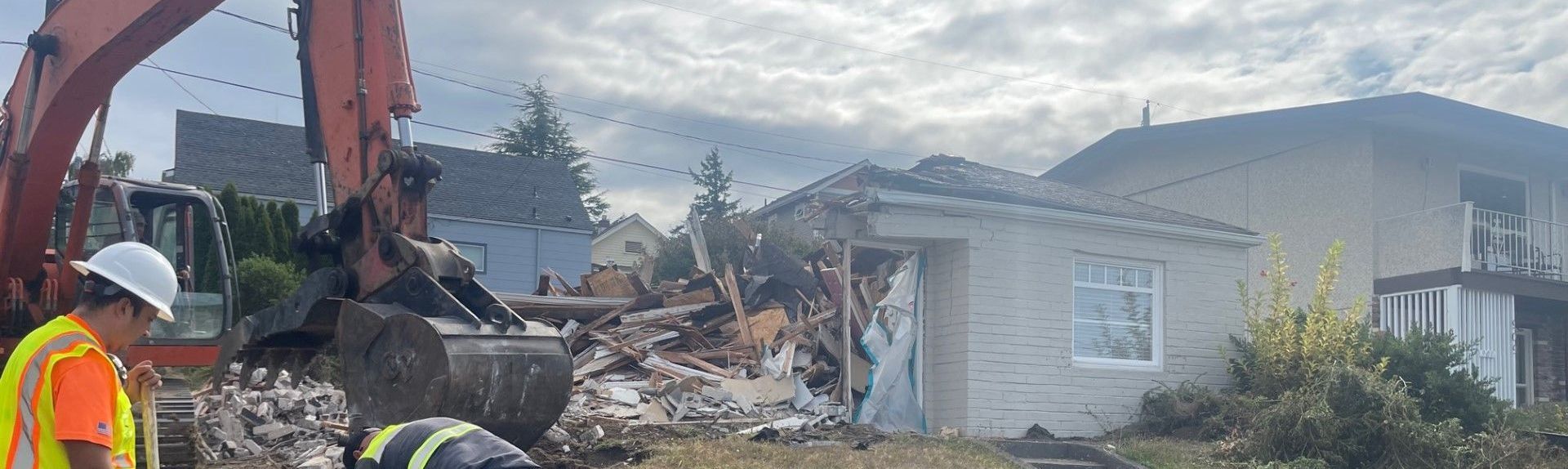 An excavator demolishes a building as construction workers observe.