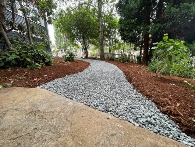 A gravel path winds through a garden, bordered by mulch and greenery.