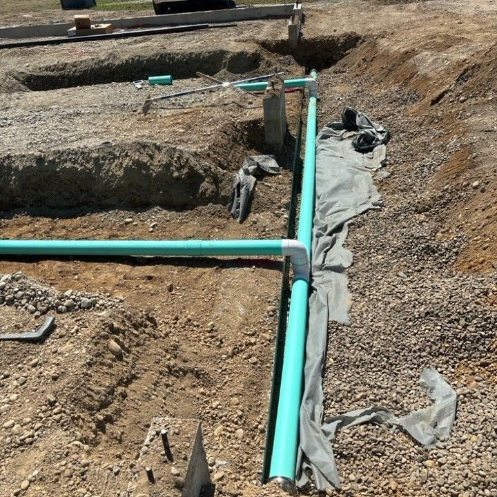Green PVC pipes in a dirt trench, connecting with white connectors; construction site.