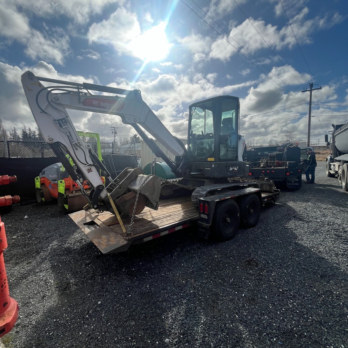 Bobcat excavator on a trailer, parked on gravel in bright sunlight.