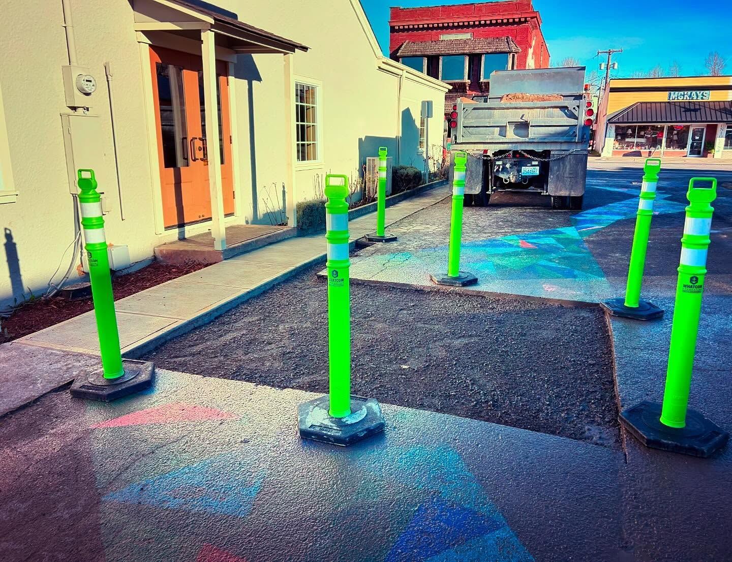 Green bollards on new asphalt surrounding a building entrance. Truck in the background.