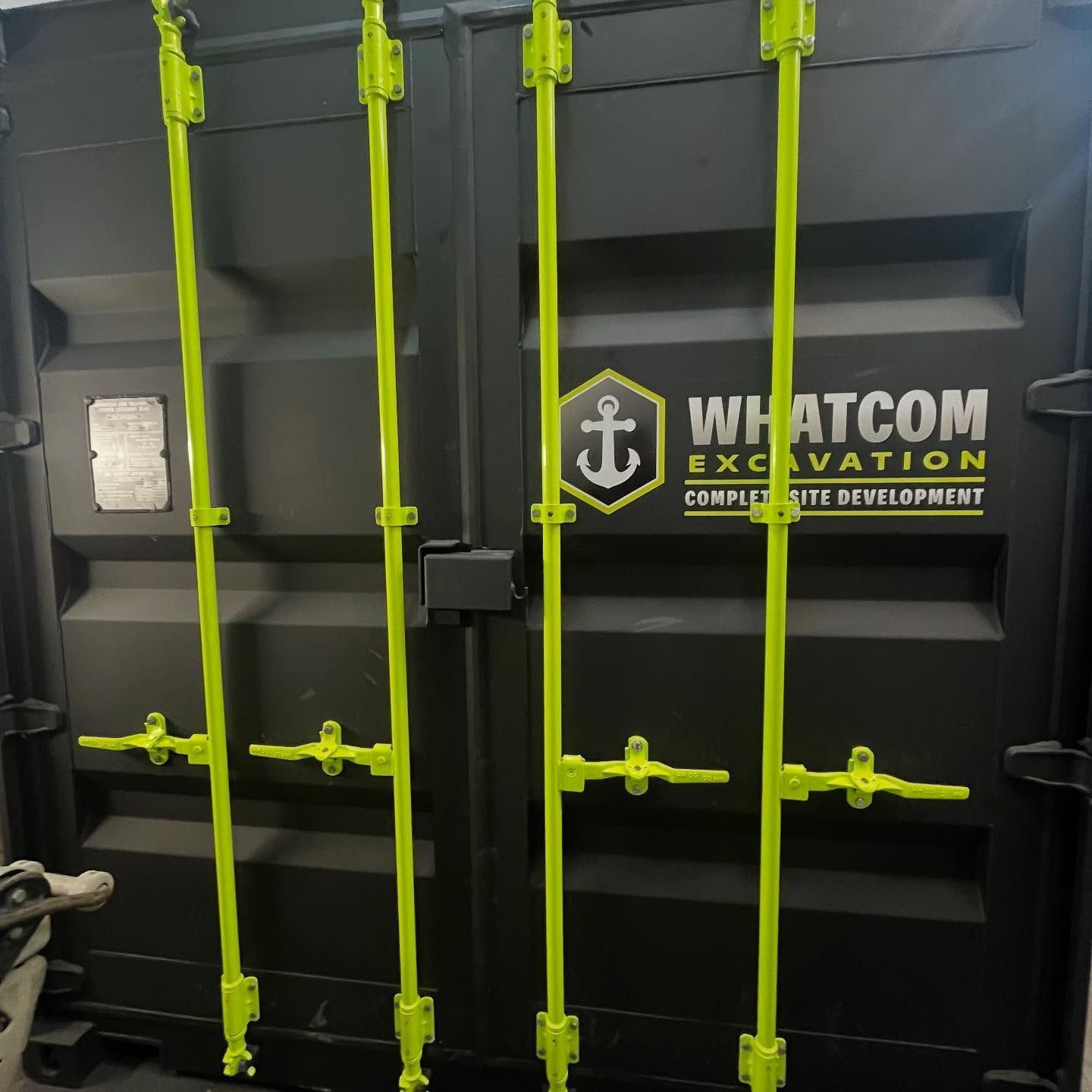 Black cargo container with bright green locking mechanisms; Whatcom Excavation logo visible.