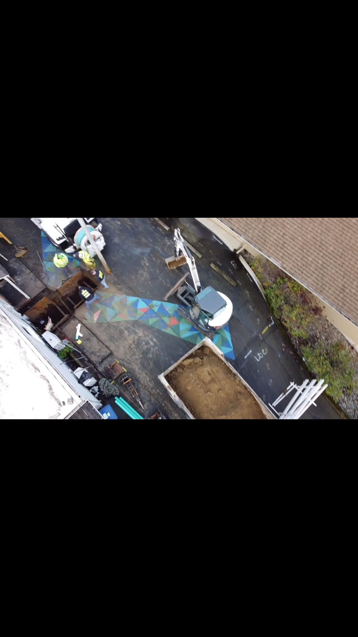 Overhead view of a cluttered alleyway; trash, a mattress, and a white appliance sit next to a building.