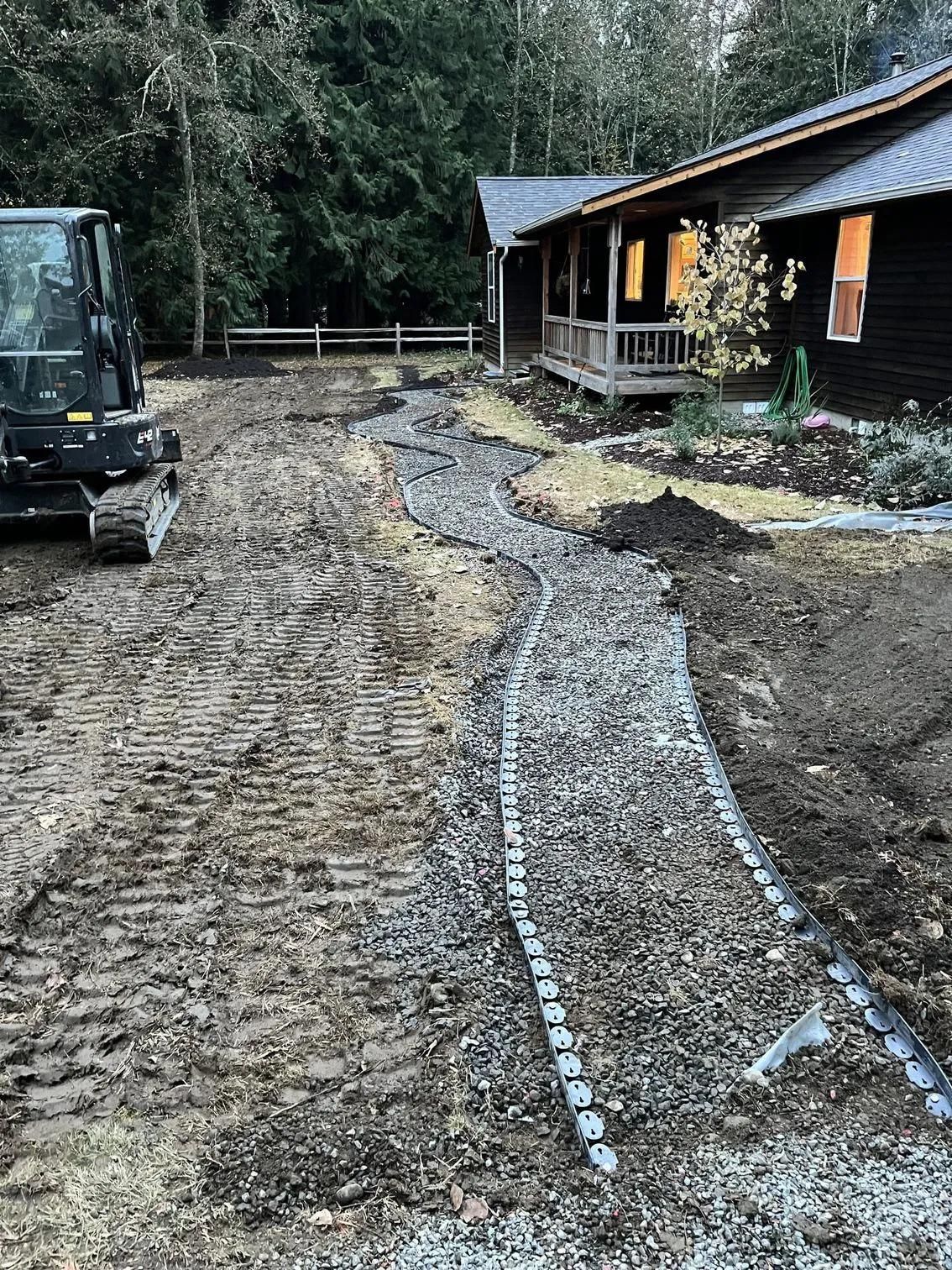 Construction site: Excavator beside a gravel path being laid out near a house.