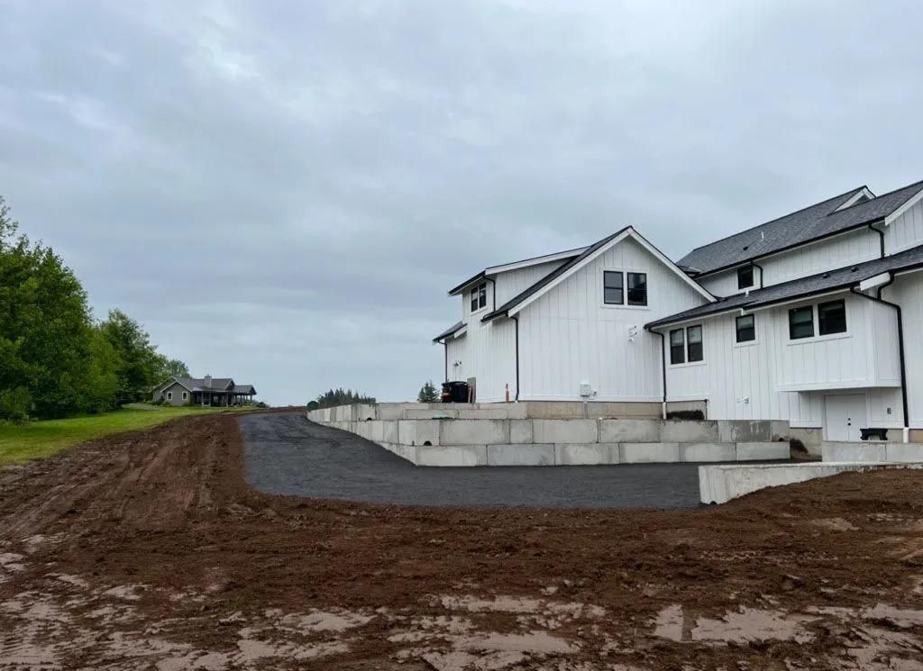 White house under cloudy sky; gravel driveway, muddy foreground, retaining wall.