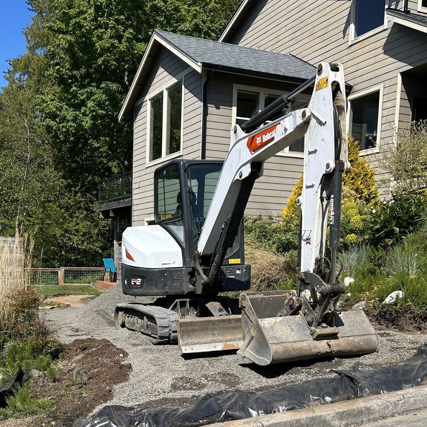 Bobcat excavator on gravel in front of a house, performing construction.
