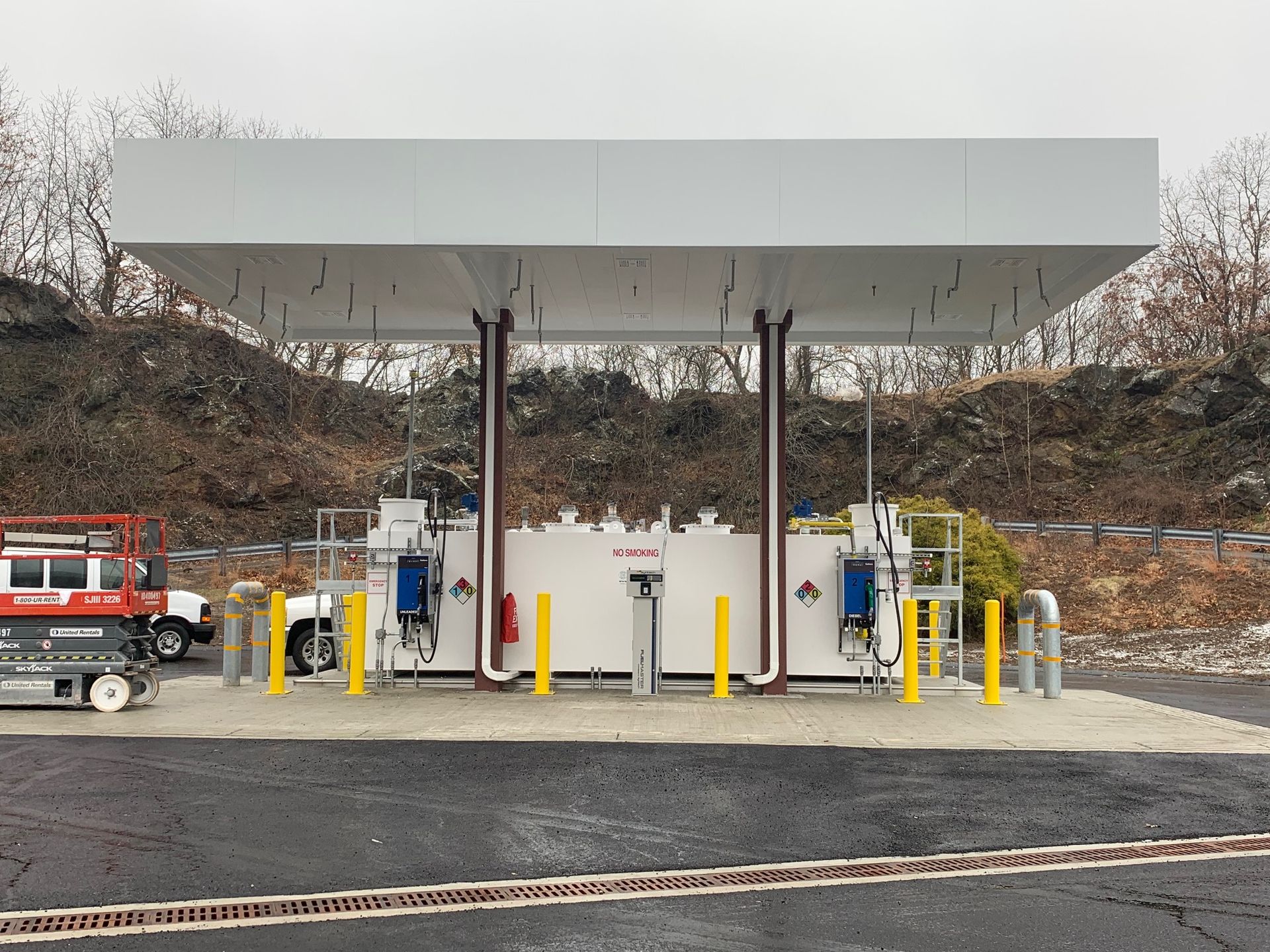A white gas station with yellow poles and a truck parked next to it