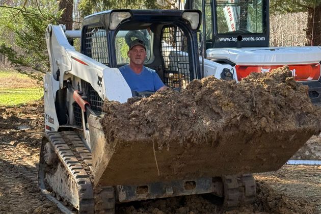 Skid steer loader dumping a bucket of dirt on a wooded worksite