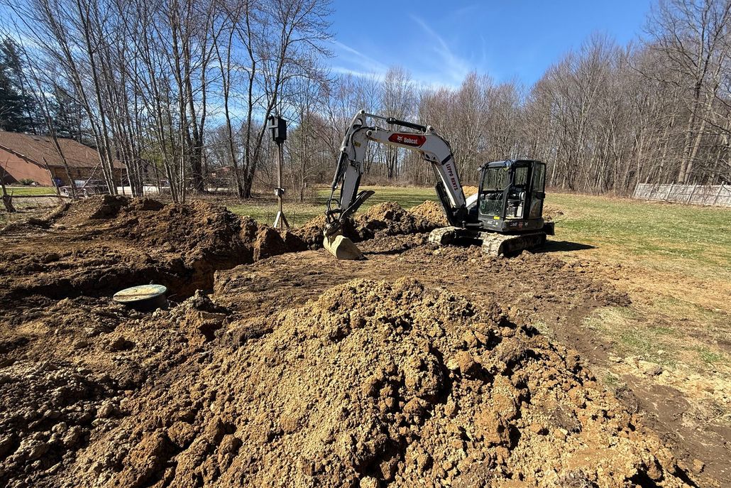 Excavator digging a large muddy trench in a wooded field on a sunny day