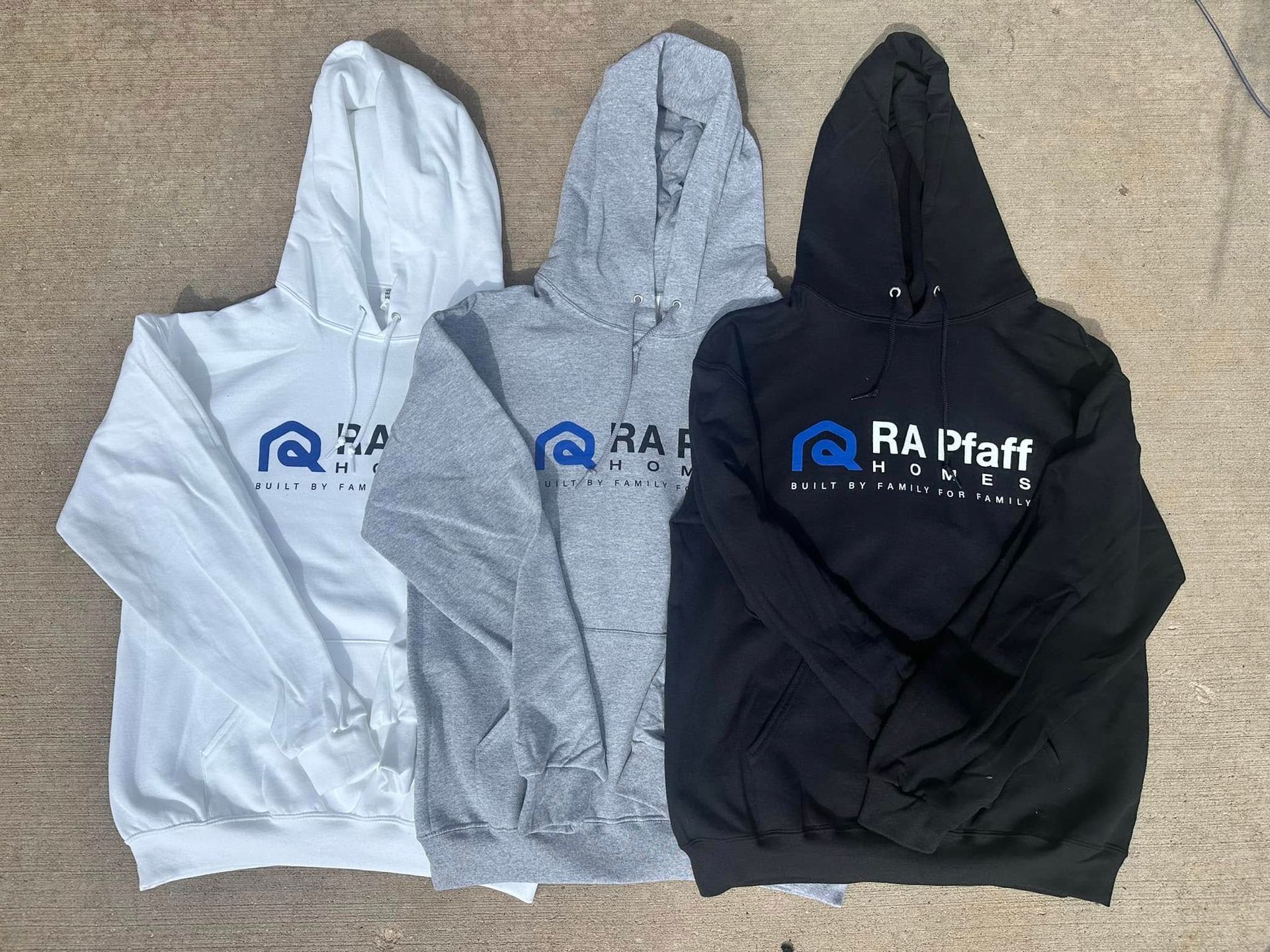 Three hooded sweatshirts, white, gray, and black, with a company logo on the front.
