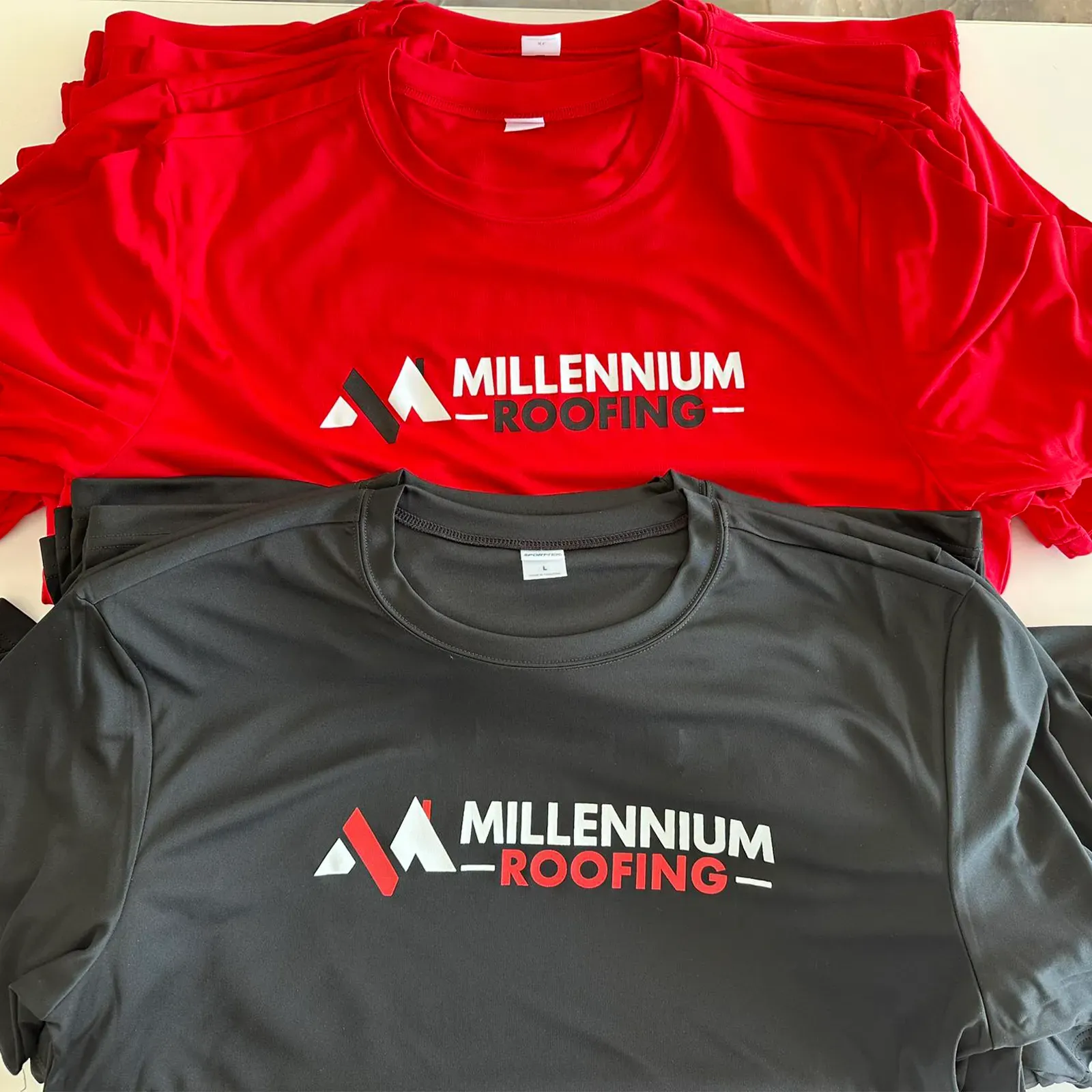 Two Millennium Roofing t-shirts: red and gray, logo on front.