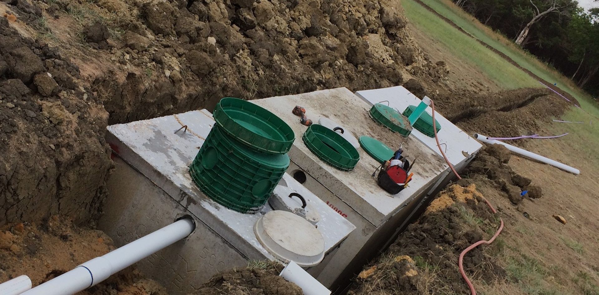 A septic tank installation with green covers and pipes on a hillside with exposed dirt.