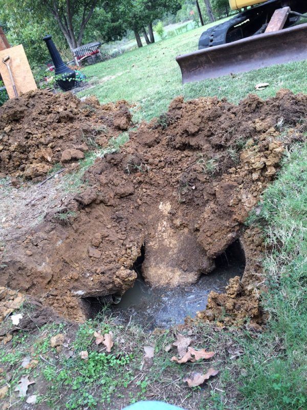 A dug-out pit with water, surrounded by dirt mounds and green grass in an outdoor setting.