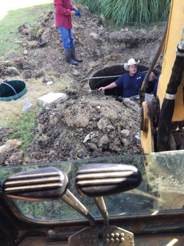 Men working on an underground structure near an excavator. One man is in the hole, another standing above.