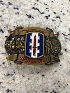 Senior OTC belt buckle with blue, white, and red shield emblem on a speckled countertop