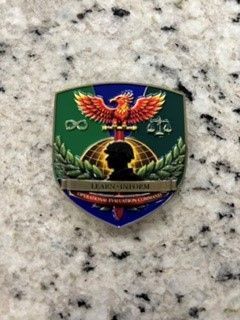 Green shield-shaped emblem with a colorful eagle and gold lettering on a speckled stone surface