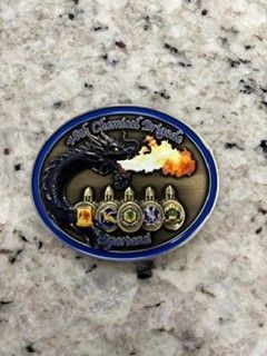 Small oval black-and-blue commemorative pin with a flaming engine and several emblems on a speckled countertop