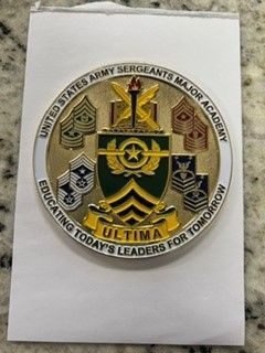 Embroidered U.S. Army Sergeant Major Academy emblem on white paper, in gold, black, green, and tan