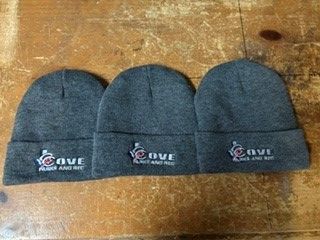 Three dark gray knit beanies with logo patches laid side by side on a wooden surface.