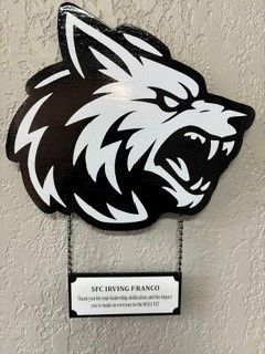 Black and white wolf mascot logo mounted on a wall above a small name plaque