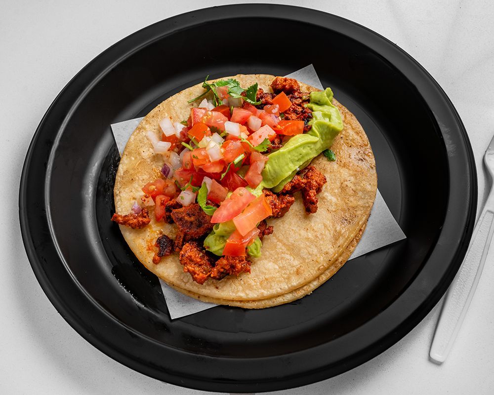 Taco on a black plate with chorizo, guacamole, and pico de gallo.