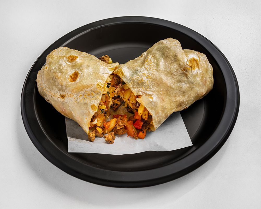 Burrito, cut open on a black plate, revealing fillings of chicken and peppers.