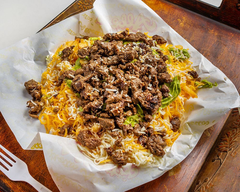 Dish of meat and cheese on a white paper, with a fork to the side.